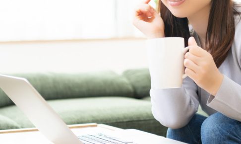 パソコンの前でコーヒーを持っている女性